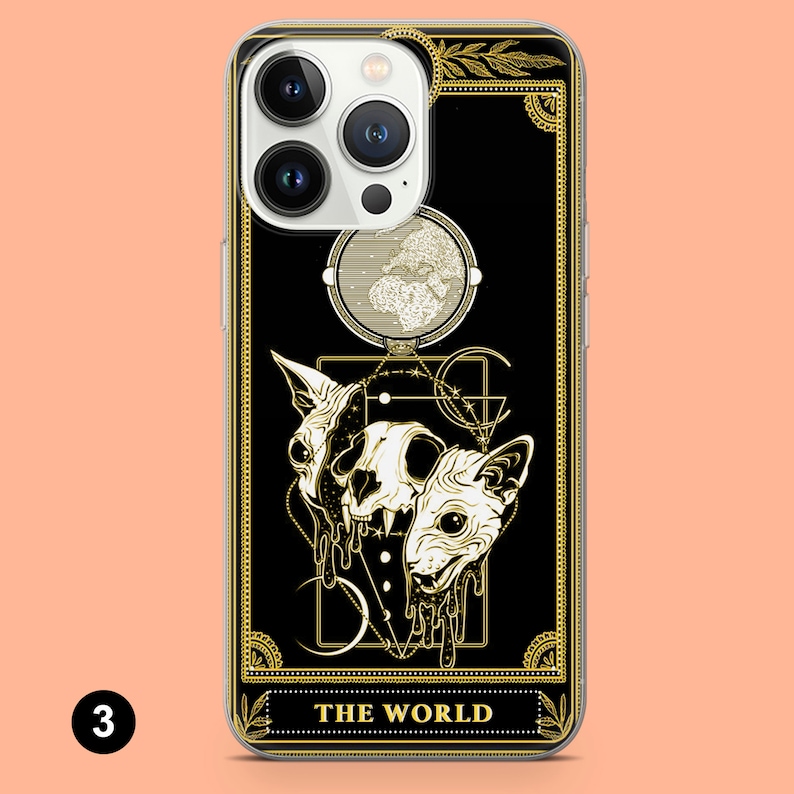 May include: A black phone case with a gold design featuring a tarot card with the number 3 and the words "THE WORLD". The card depicts a skull with two cat heads, a crescent moon, and a circle with stars.