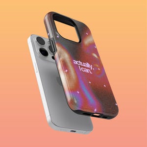 以下が含まれることがあります： キラキラと光る抽象的なデザインと「actually, I can.」というピンクの文字が書かれた携帯電話ケースです。