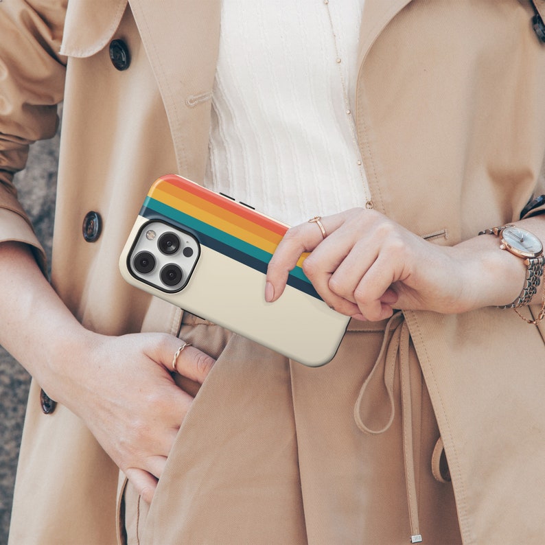May include: A white iPhone case with a colorful rainbow stripe design. The case has a raised camera bump and a cutout for the phone's buttons.