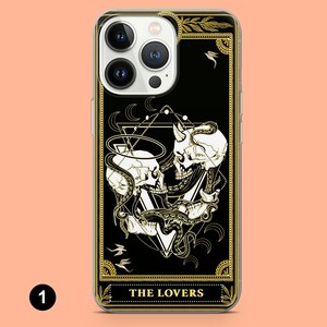 May include: A black and gold iPhone case with a tarot card design featuring two skulls intertwined with an octopus. The card is titled "The Lovers".