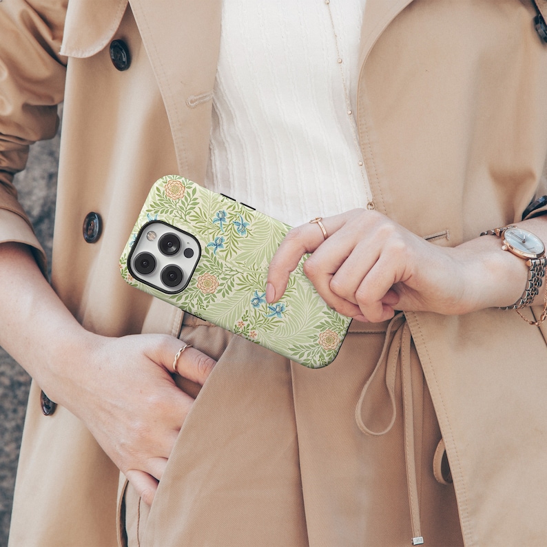 May include: A green and white floral phone case with a blue floral pattern. The case is designed for an iPhone with a camera lens visible.