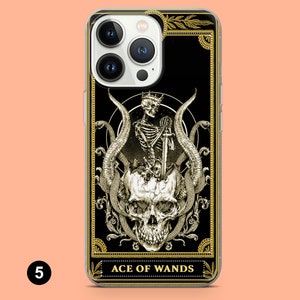 May include: A black and gold iPhone case with a tarot card design featuring a skeleton holding a sword and a skull with snakes. The card reads "Ace of Wands".