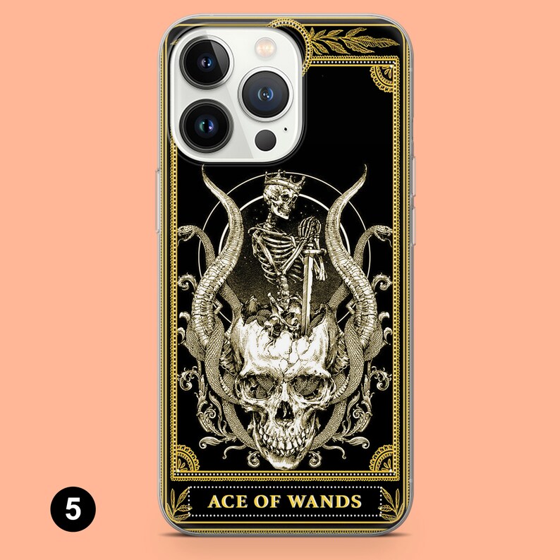 May include: A black and gold iPhone case with a tarot card design featuring a skeleton holding a sword and a skull with snakes. The card reads "Ace of Wands".
