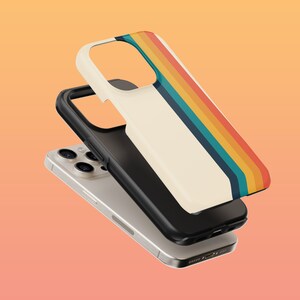 May include: A white phone case with a retro rainbow stripe design. The case is shown on top of a silver iPhone with a camera lens.