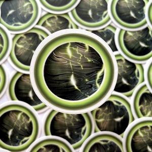May include: A close-up of a green and black sticker with a lightning bolt design. The sticker is round and has a white border. There are many other stickers in the background.