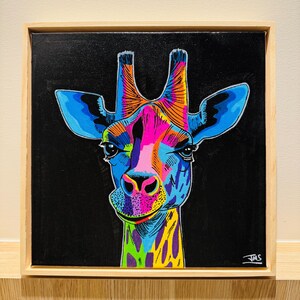 May include: A vibrant, pop art style painting of a giraffe's head against a black background. The giraffe is rendered in bright colors including blue, pink, orange, and yellow. The artwork is framed in a natural wood frame.