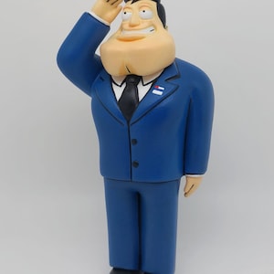 Puede incluir: Una figurita azul y blanca de un personaje de dibujos animados que lleva un traje azul, camisa blanca y corbata negra. El personaje está saludando con la mano derecha y tiene una gran sonrisa.