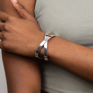 May include: A silver bangle bracelet with a criss-cross design. The bracelet is open and adjustable.