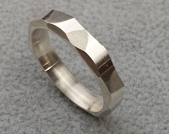 May include: A silver ring with a faceted, geometric design. The ring has a brushed finish and a slightly rounded edge.