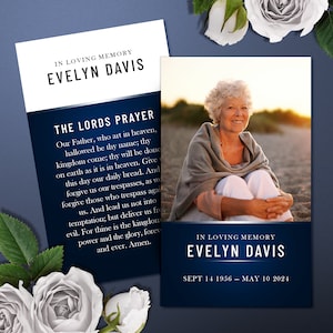 May include: A blue and white memorial card with a photo of a woman sitting on a beach. The card reads "In Loving Memory Evelyn Davis" and includes the text of the Lord's Prayer. The dates "Sept 14 1956 - May 10 2024" are printed at the bottom.