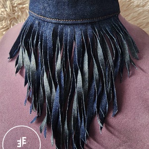 May include: A denim choker necklace with a fringe trim. The fringe is made of denim and is about 3 inches long. The choker is a dark blue color and has a brown stitching detail.