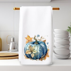 May include: A white kitchen towel with a blue and yellow watercolor pumpkin design. The pumpkin is surrounded by leaves and vines.