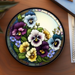 May include: A round ceramic plate with a colorful floral design featuring purple, yellow, and white pansies. The plate has a white background with a light blue border.