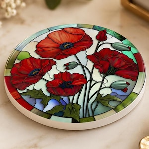 May include: A circular coaster featuring a stained glass style design of vibrant red poppy flowers with green stems and leaves against a light blue and white background, enclosed within a decorative border of green and red glass segments.