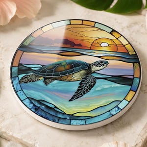 May include: A round ceramic coaster featuring a stained glass style illustration of a sea turtle swimming in ocean water. The design includes a sunset sky with orange and yellow hues, blue waves, and a dark-colored turtle with detailed shell patterns.