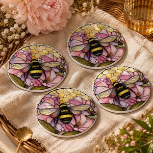 Four round ceramic coasters with identical bumblebee and pink floral designs arranged on a fabric-lined tray.
