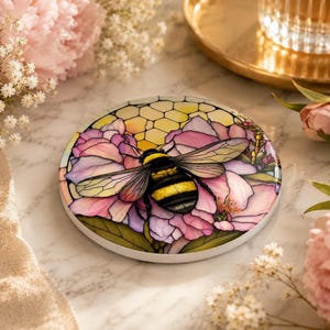 A single circular ceramic coaster with a stained-glass style bumblebee and pink flower design resting on a marble surface.