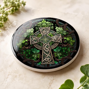 A single round ceramic coaster with a green Celtic cross and ivy design, on a light speckled surface with green ivy leaves.