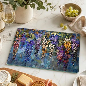 A rectangular glass cutting board with a wisteria art pattern in shades of purple, blue, green, and yellow, surrounded by cheese, crackers, and grapes.