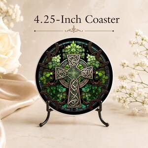 A 4.25-inch ceramic coaster with a green Celtic cross and ivy design, displayed upright on a black metal stand, with white roses in the background.