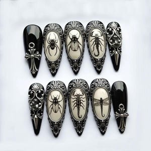 May include: A set of ten black and silver gothic-style false nails. Each nail features a different design, including insects like spiders, beetles, and scorpions, set within ornate silver frames. Two nails have a cross design.