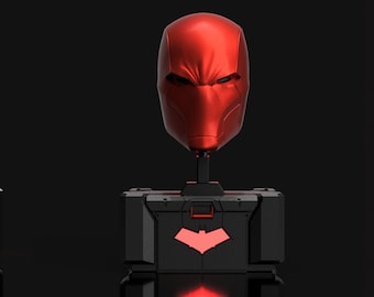 May include: Red Hood bust with a black base and a red light. The bust is made of a smooth, glossy material. The base has a raised bat symbol. The text "THE PROP SHOP Lnd" is visible on the base.