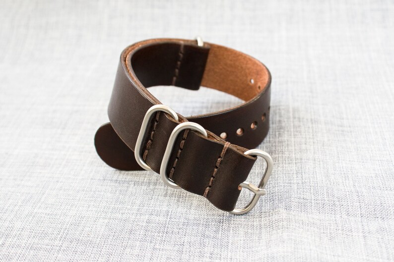 Puede incluir: Una correa de reloj de cuero marr&oacute;n con herrajes plateados. La correa tiene un borde cosido y est&aacute; dise&ntilde;ada para un reloj con una anchura de leng&uuml;eta de 20 mm.