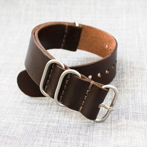 Puede incluir: Una correa de reloj de cuero marr&oacute;n con herrajes y costuras plateadas. La correa tiene varios agujeros para ajustar el ajuste.