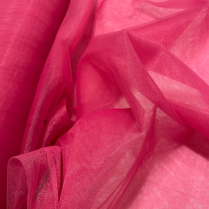 May include: A close-up of a roll of bright pink sheer fabric. The fabric is translucent, with visible folds and textures. The colour is a vibrant, saturated pink, creating a visually appealing display of textiles.