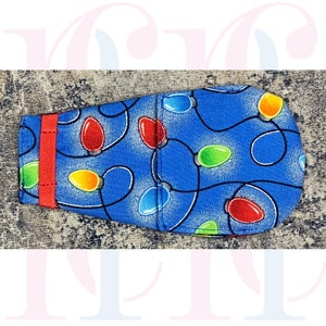 May include: Blue fabric with a pattern of colourful Christmas lights. The fabric has a red trim on one side.