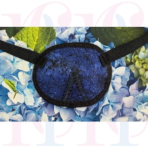 May include: A blue eye patch with a black border and strap. The eye patch features a blue floral pattern. The background shows a floral pattern of blue and green flowers. The eye patch is designed to cover one eye.