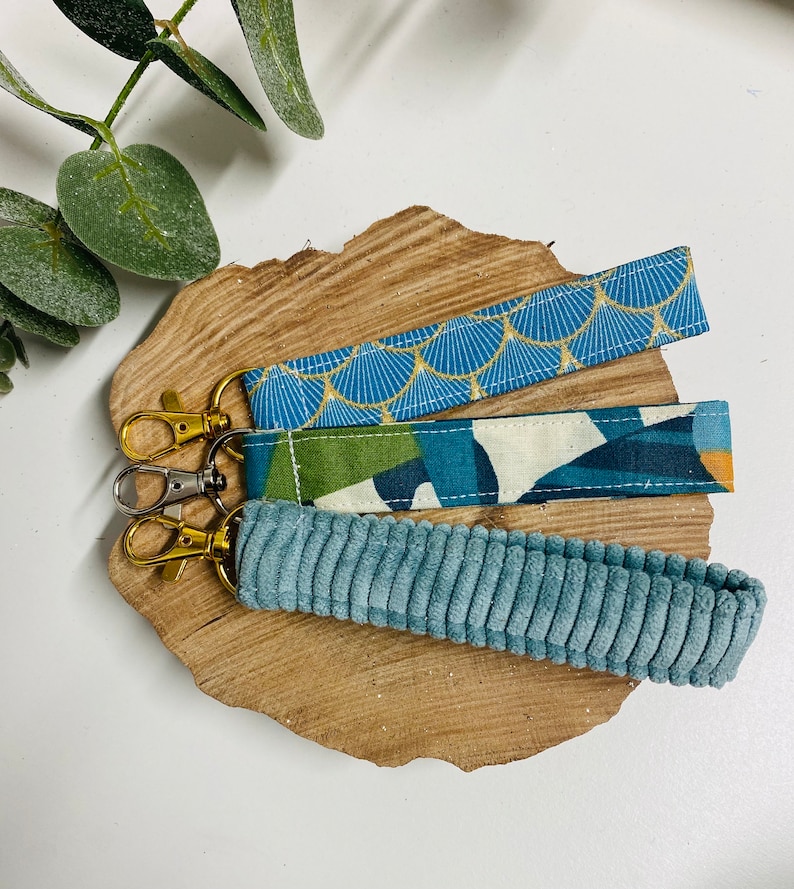 K&ouml;nnte beinhalten: Drei Schl&uuml;sselanh&auml;nger mit verschiedenen Stoffmustern. Der obere Schl&uuml;sselanh&auml;nger ist blau mit einem goldenen geometrischen Muster. Der mittlere Schl&uuml;sselanh&auml;nger ist gr&uuml;n, wei&szlig; und blau mit einem geometrischen Muster. Der untere Schl&uuml;sselanh&auml;nger ist aus einfarbigem blauem Cord.