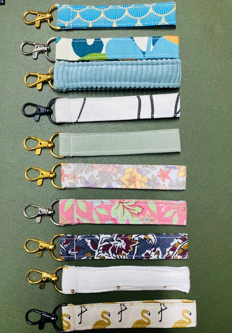 K&ouml;nnte beinhalten: Ein Set mit 10 bunten Stoffschl&uuml;sselanh&auml;ngern mit goldenen und silbernen Schl&uuml;sselringen. Die Schl&uuml;sselanh&auml;nger zeigen eine Vielzahl von Mustern, darunter florale, geometrische und abstrakte Designs.
