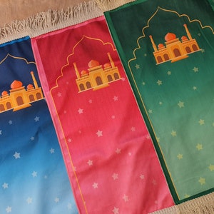 May include: Three prayer rugs with fringe edges. The rugs are blue, pink, and green with a gold mosque design and white stars.