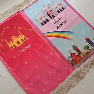 May include: Two pink prayer rugs with fringe trim. One rug features a mosque with a rainbow and the name Amelia. The other rug features a mosque and stars with the name Amelia.