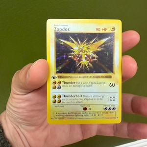 May include: A yellow Zapdos Pokémon trading card. The card features a stylized illustration of Zapdos, a legendary electric-type bird. The card text includes the Pokémon's HP, attacks, and other game details. The card is 1.60m long and weighs 52.6 kg.
