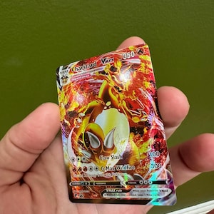May include: A Charizard VMAX trading card with a fiery design. The card features a large orange and red dragon with the text "Charizard VMAX" and "Claw Slash". The card has a holographic finish.