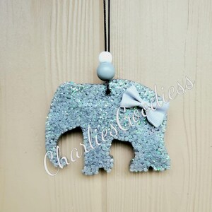 May include: A gray glitter elephant car air freshener with a gray bow and white beads on a black string.