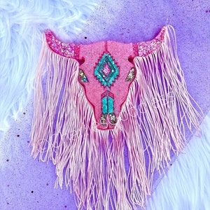 May include: Pink glitter cow skull with turquoise and pink geometric design and pink fringe.