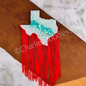 May include: White resin Texas state outline with turquoise and gold glitter, red fringe hanging from the bottom.  ©Charlie's Goodies