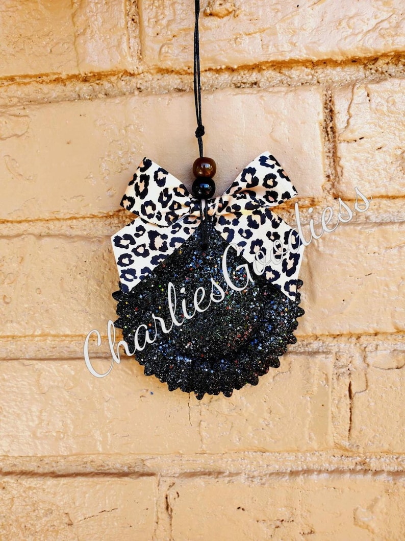 May include: Black and white leopard print fabric bow tied to a black glitter circle car air freshener with a black string.