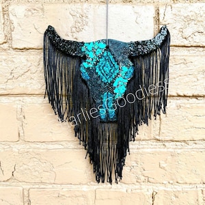 May include: Black and turquoise glitter bull skull with black fringe hanging from a brick wall.