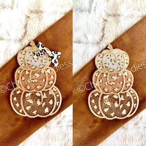 May include: A stack of three wooden pumpkins decorated with a leopard print pattern and gold glitter. The pumpkins are stacked on top of each other and have a rustic, farmhouse style.