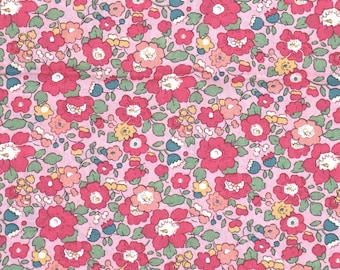 Pode incluir: Um tecido rosa com um padrão repetitivo de pequenas flores vermelhas, cor-de-rosa e amarelas. As flores são cercadas por folhas verdes.