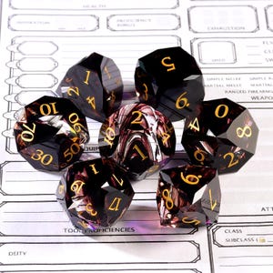May include: Set of seven polyhedral dice with a dark, translucent appearance and gold numbering. The dice have a marbled, swirling pattern in shades of burgundy and cream. The dice are designed for tabletop role-playing games and are displayed on a game sheet.
