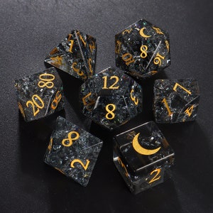 May include: Set of eight black and gold dice with a glittery finish. The dice are numbered 1 through 8 and feature a crescent moon symbol on one side.