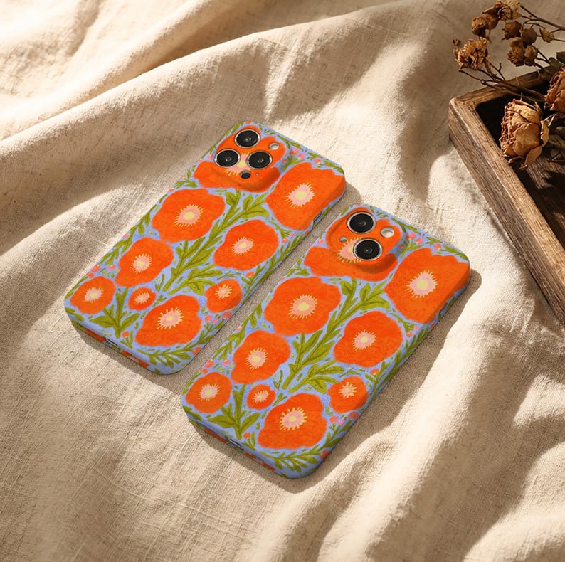 Puede incluir: Dos fundas rectangulares para tel&eacute;fono con un patr&oacute;n vibrante de flores de amapola de color naranja brillante con centros amarillos y tallos verdes sobre un fondo azul b&iacute;garo claro. Cada funda tiene recortes precisos para las lentes.