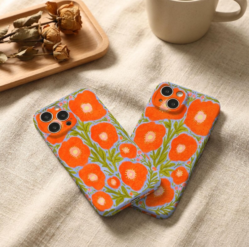 Puede incluir: Dos fundas rectangulares para smartphone con un vibrante estampado floral de amapolas de color naranja brillante con centros amarillos y tallos verdes sobre un fondo azul b&iacute;garo claro. Las fundas tienen recortes para las lentes.