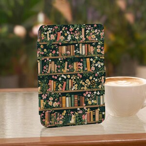 May include: A rectangular tablet case featuring a dark green background with a repeating pattern of wooden bookshelves filled with various books and interspersed with colourful flowers, including pink, white, and yellow blossoms.