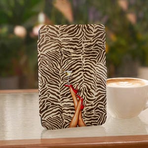 May include: A rectangular tablet case featuring a brown and beige zebra print pattern. The center of the case displays an illustration of two legs wearing bright red high-heeled shoes, with one foot balancing a martini glass with an olive.